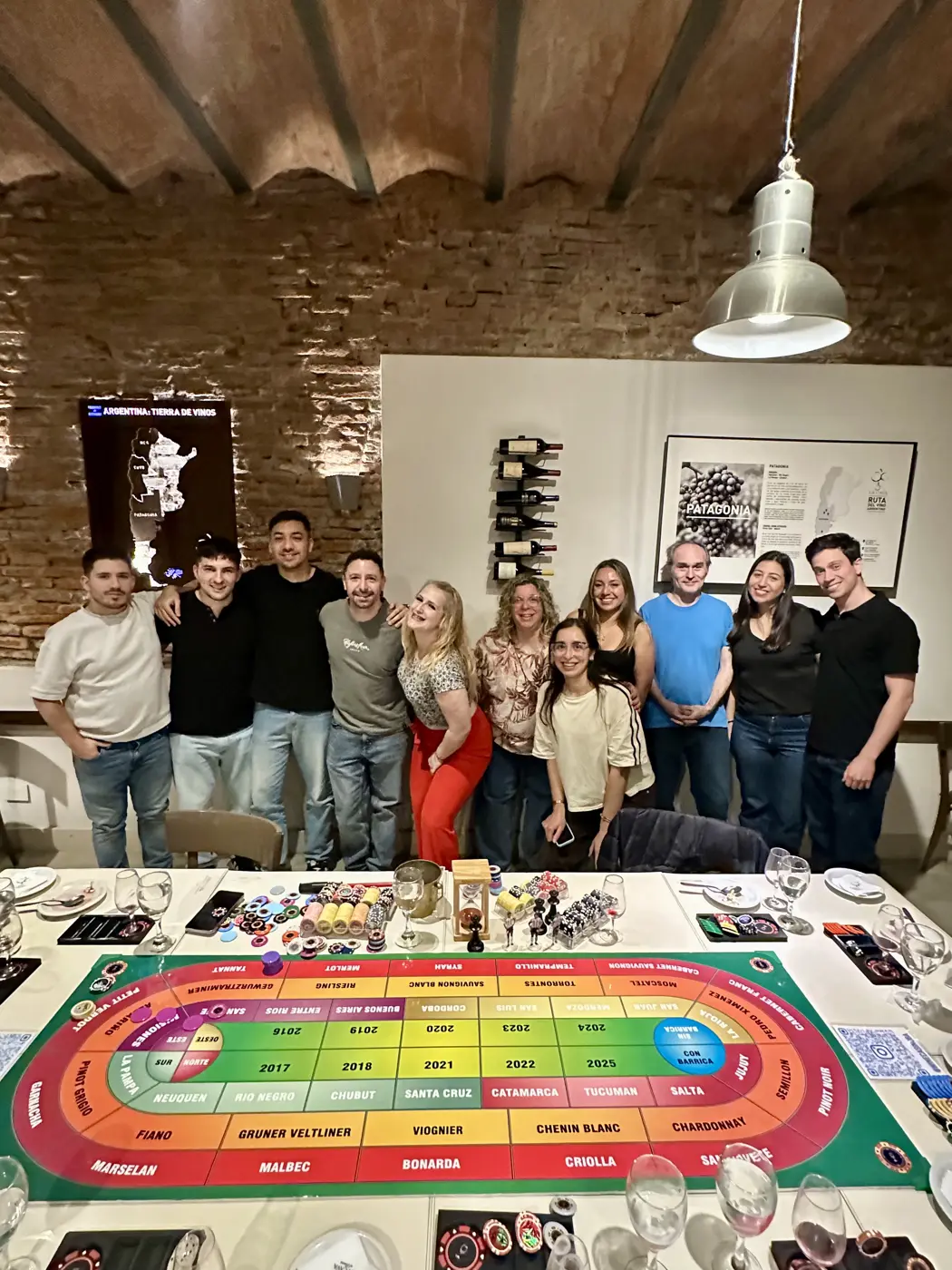 Grupo sonriendo detrás de la mesa de juego con el tablero de cepas, provincias y años