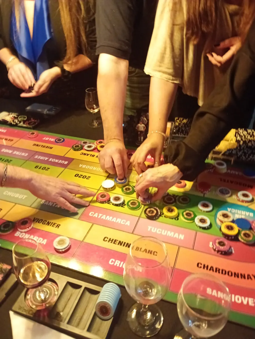 Jugadores colocando sus fichas sobre el tablero con copas de vino