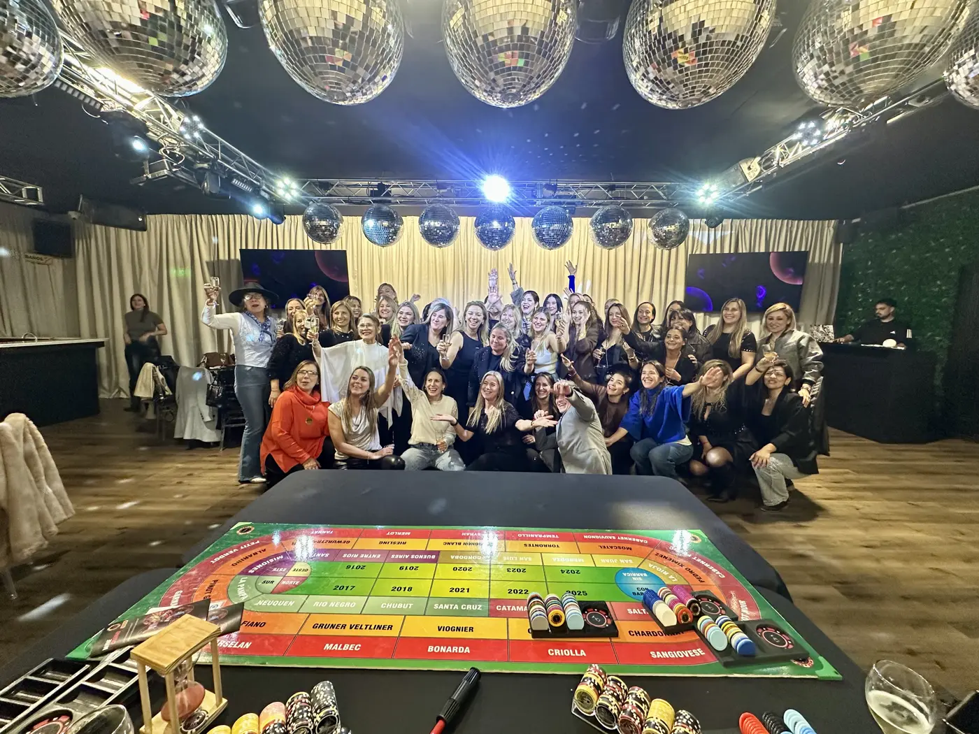 Un gran grupo festejando en un salón con bolas de espejos y el tablero en primer plano