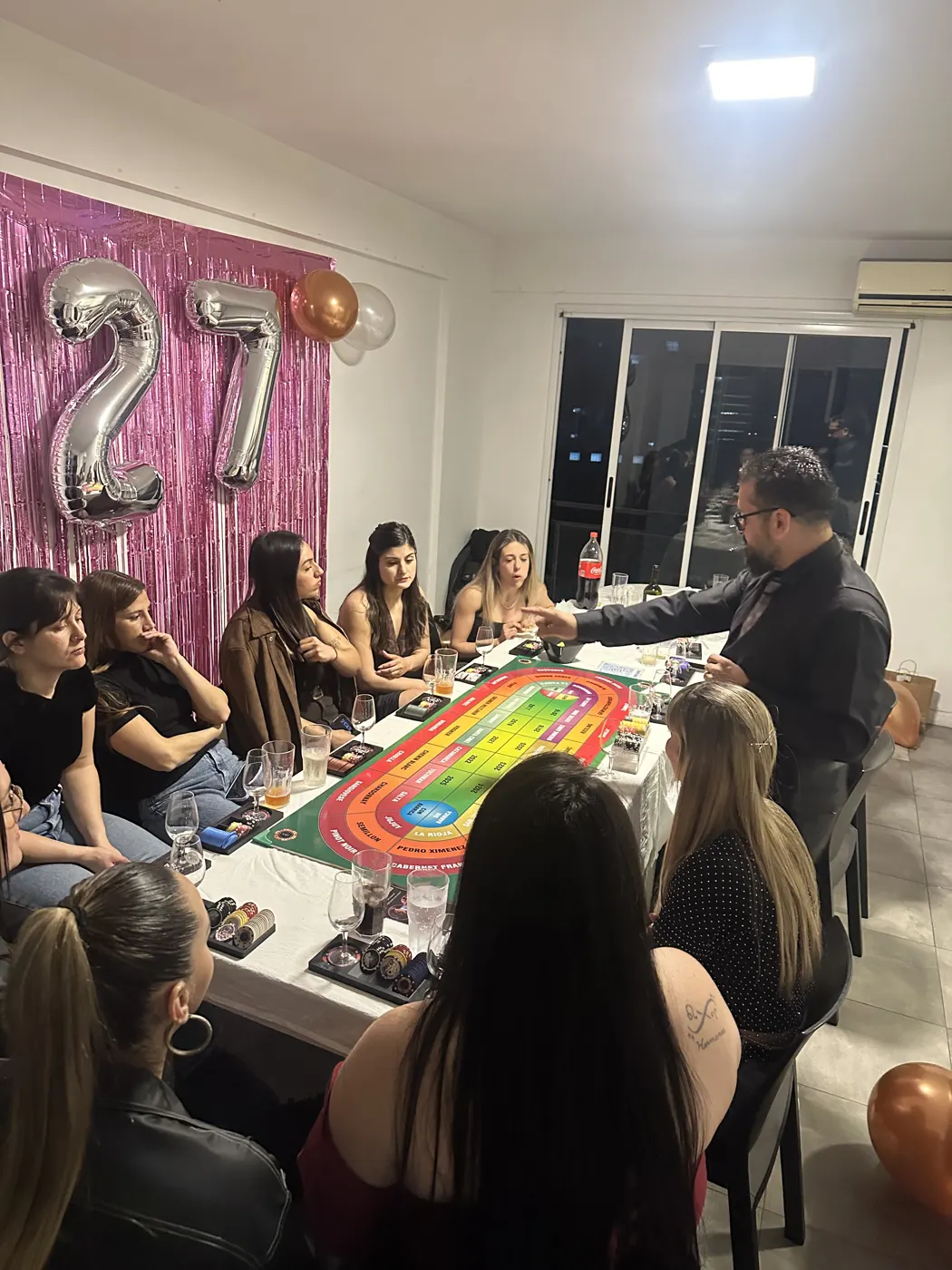 Cumpleaños con amigas alrededor del tablero de Wine Casino, con globos de fondo